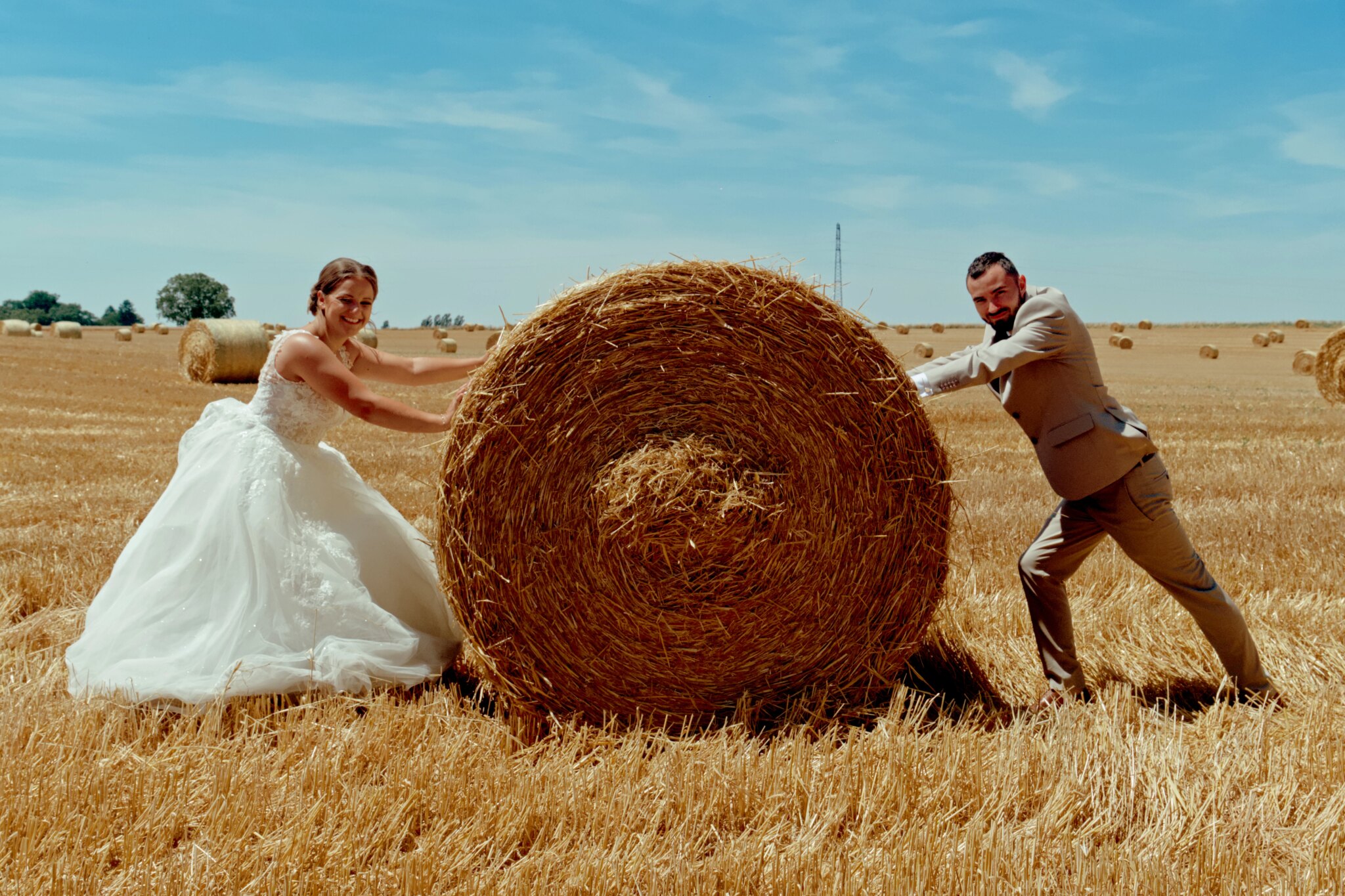 Photo des mariés dans un champ avec une botte de foin entre eux